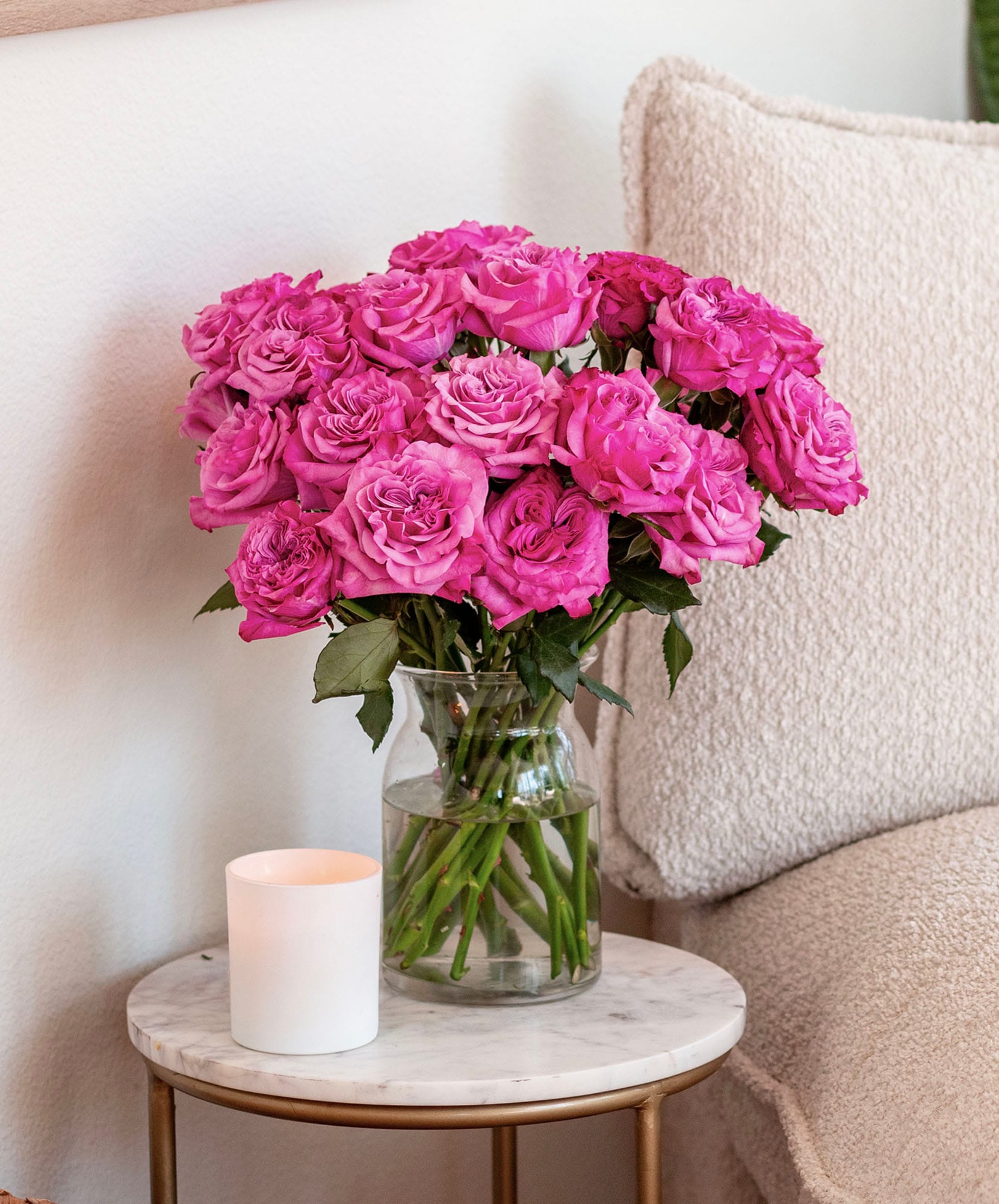 A vibrant bouquet of pink roses elegantly displayed on a marble table beside a candle.